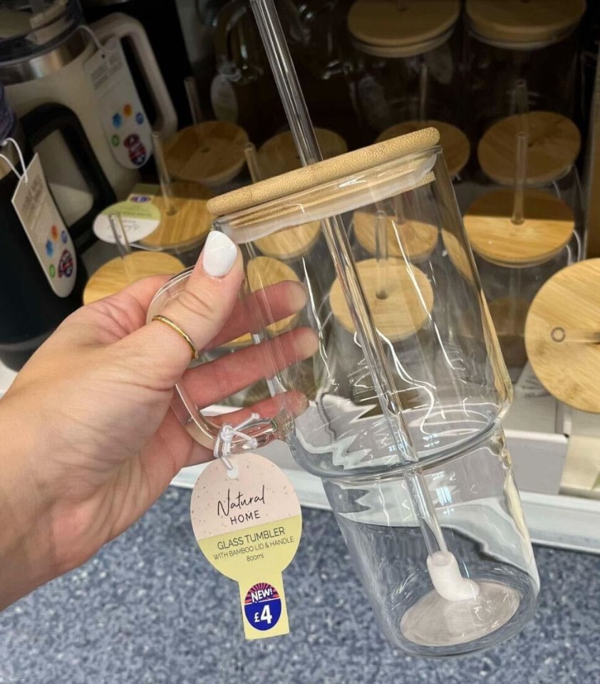 a person is holding a glass tumbler with a bamboo lid