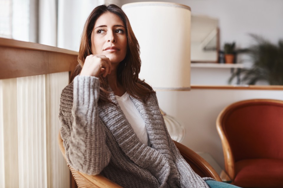 a woman in a grey sweater sits in a chair looking out a window