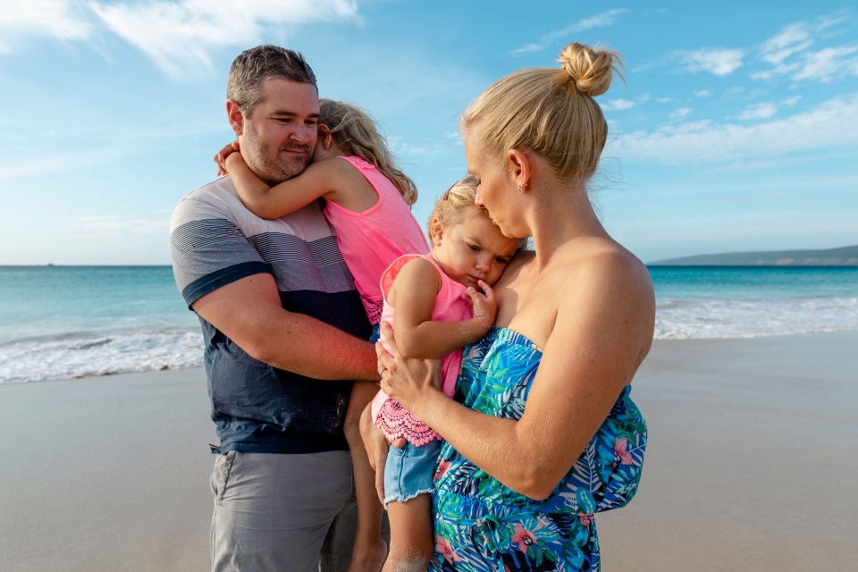 a man and woman holding a little girl on the beach