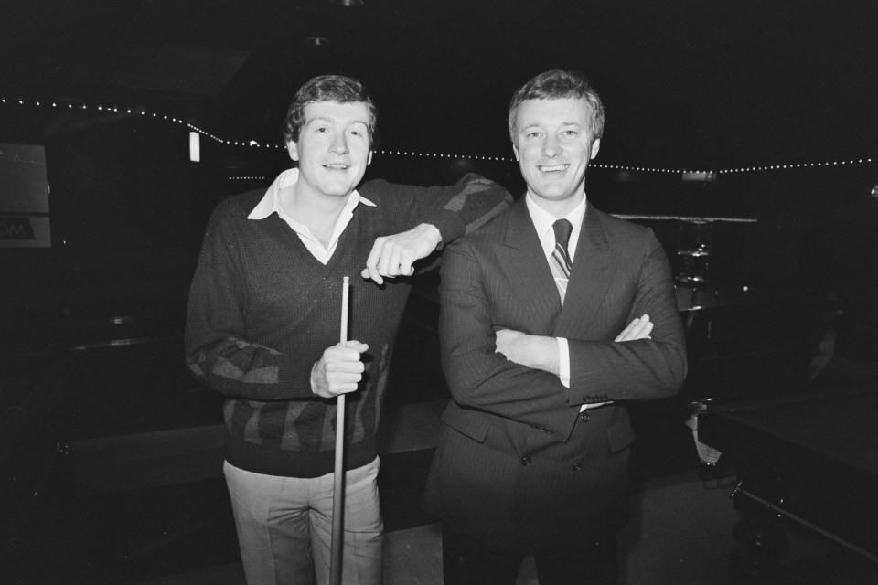 two men standing next to each other with one holding a pool cue