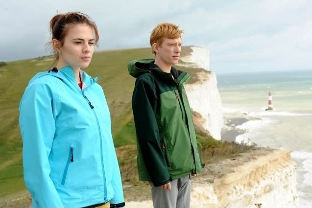 a man and a woman are standing on a cliff overlooking the ocean