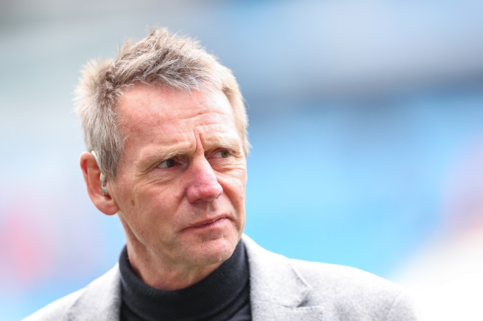 a man in a grey jacket and black turtleneck looks to the side