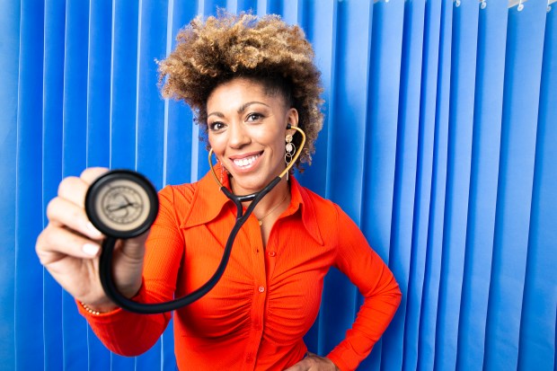 a woman in an orange shirt is holding a stethoscope in front of a blue curtain