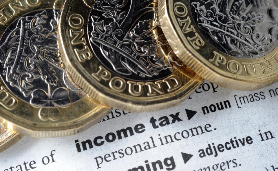 One pound coins on a dictionary page defining income tax.