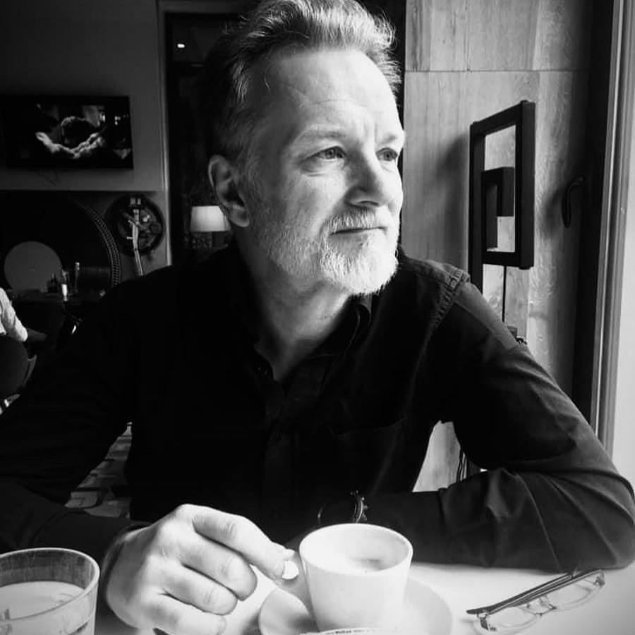 a man with a beard sits at a table with a cup of coffee