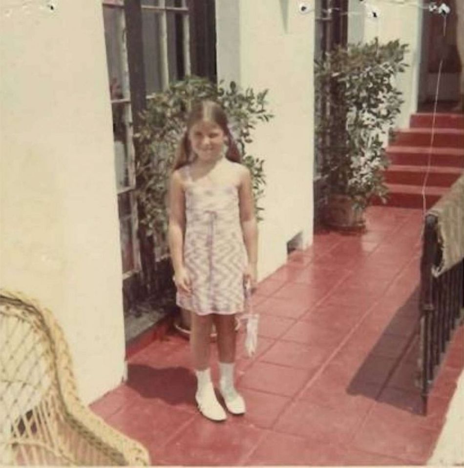 a little girl in a pink dress is standing on a red tiled porch holding an umbrella .