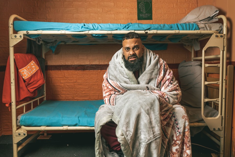 a man wrapped in a blanket sits on a bunk bed