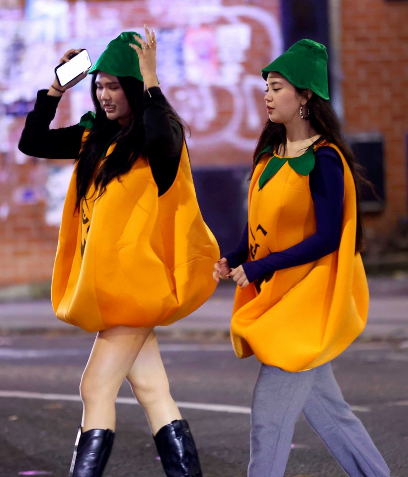 two women dressed as pumpkins are walking down the street