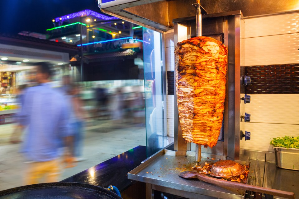 a man stands in front of a sign that says burgers kebabs