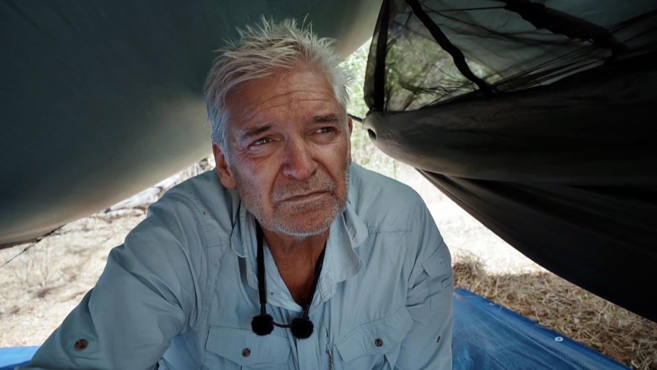 a man in a blue shirt is laying under a tent