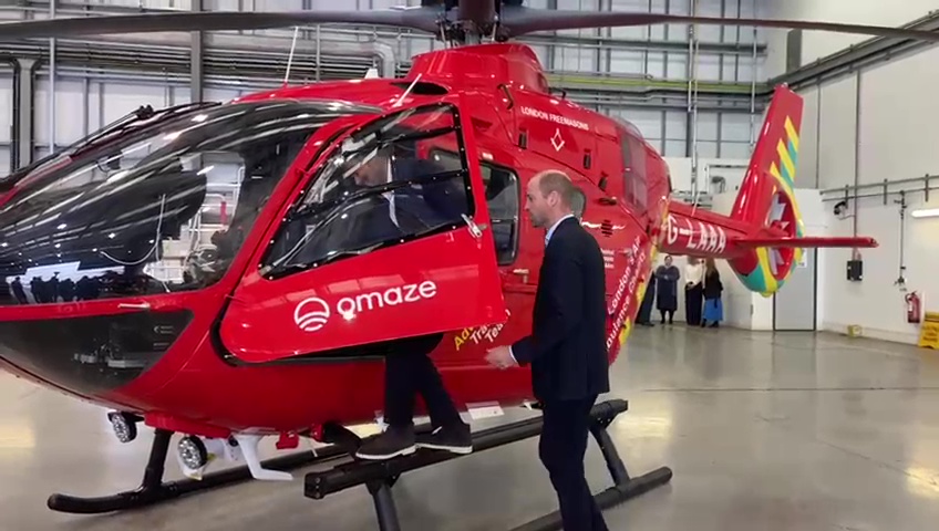 a man stands next to a red helicopter that says qmaze on the side