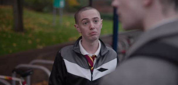 a young man wearing a jacket and tie is talking to another young man .