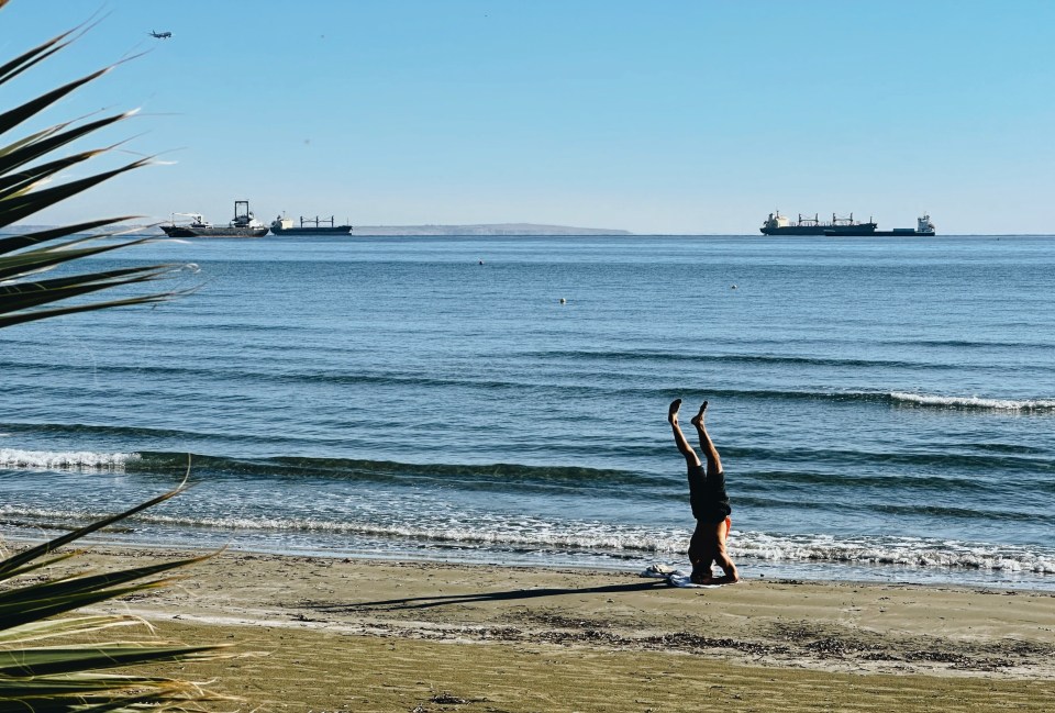 a person doing a handstand on the beach with ships in the background