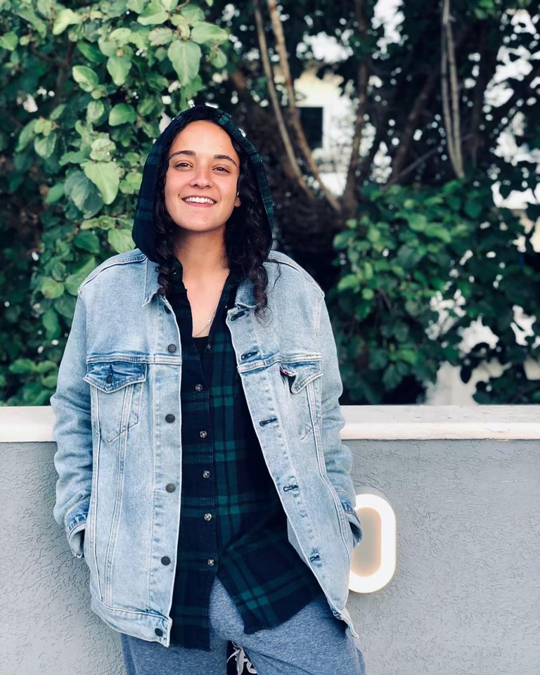 a woman wearing a denim jacket and a plaid shirt smiles for the camera