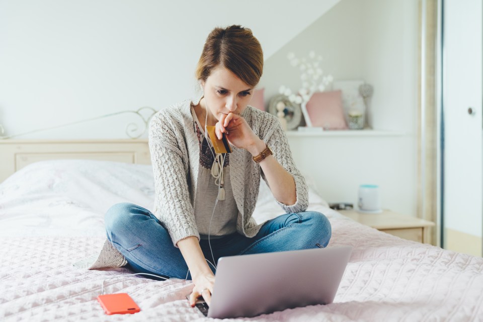 a woman sits on a bed using a laptop