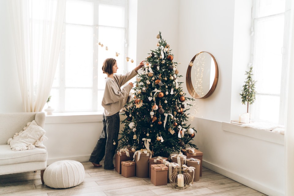 a woman decorates a christmas tree in front of a window