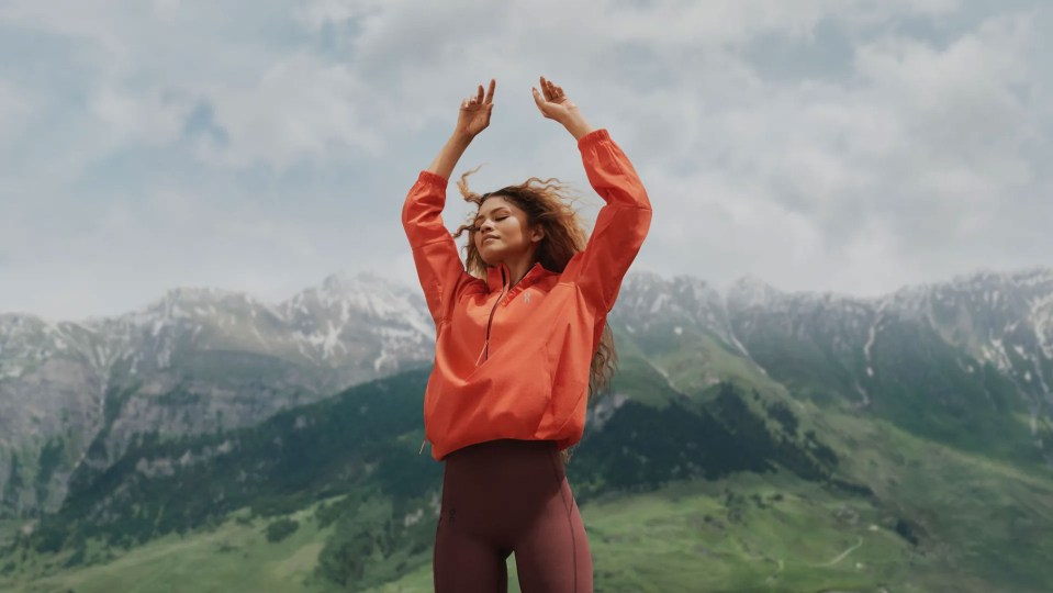 a woman in an orange jacket is standing in front of a mountain