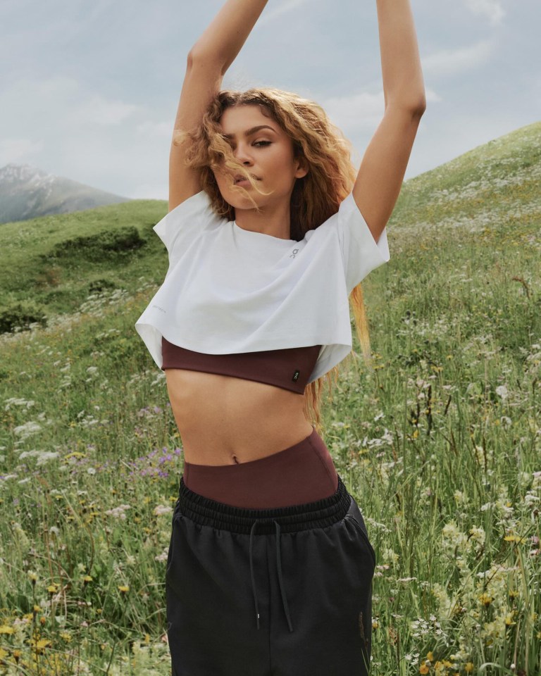 a woman in a white crop top and black shorts stands in a field of flowers