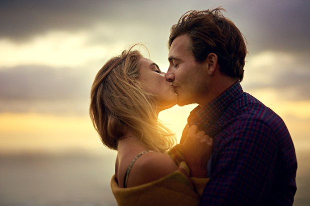 a man and a woman kissing in front of a cloudy sky