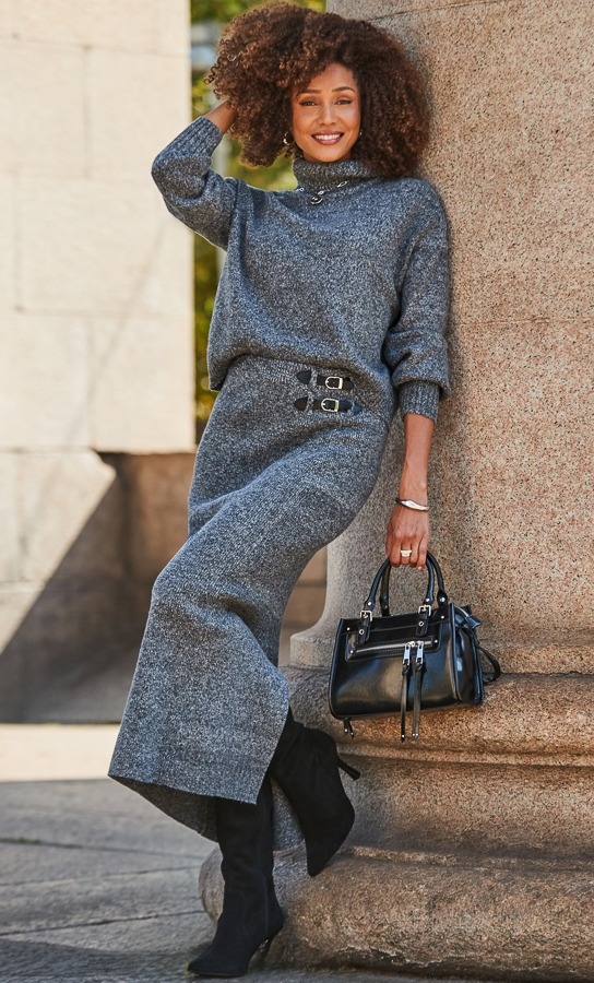 a woman wearing a grey sweater and skirt is holding a black purse