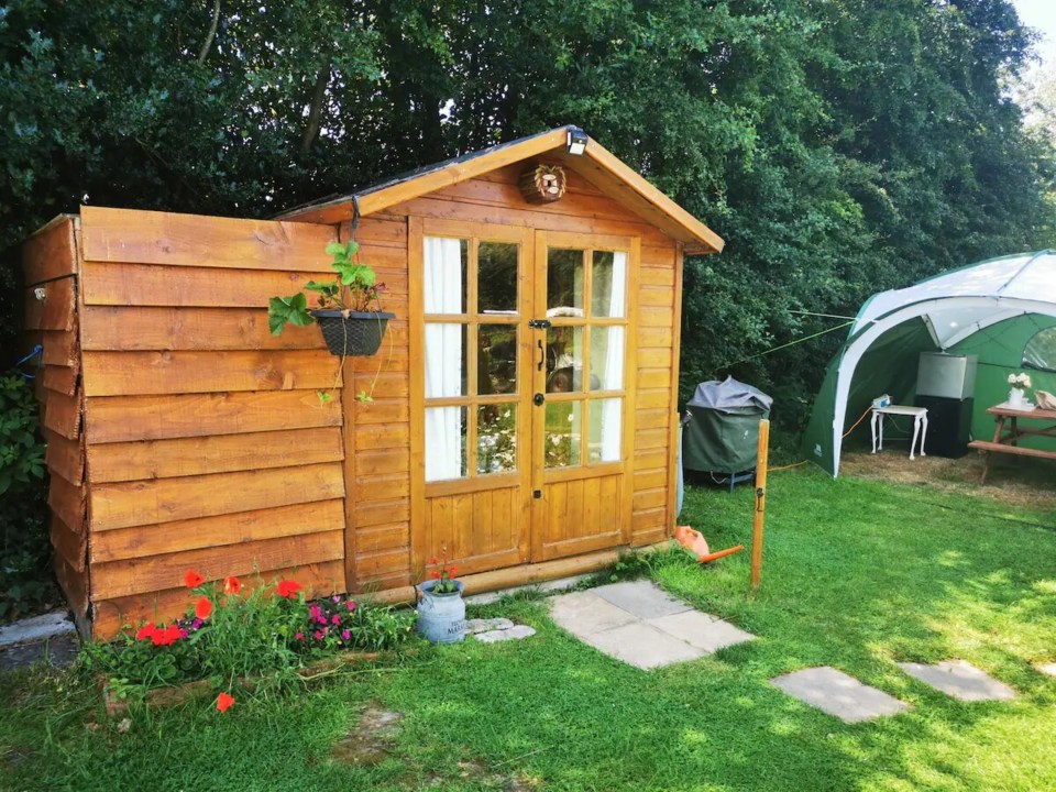 a wooden shed in a backyard with a green tent in the background