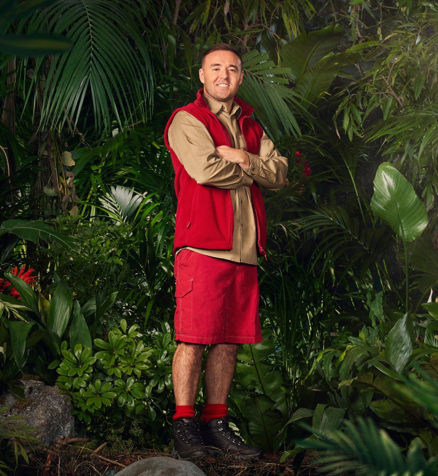 a man in a red vest stands in a jungle with his arms crossed