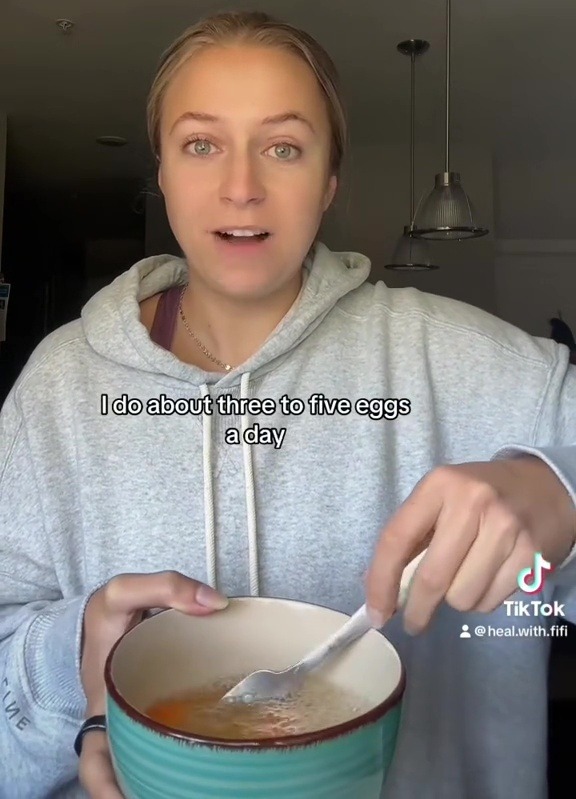 a woman in a grey hoodie is holding a bowl of food with the caption " i do about three to five eggs a day "