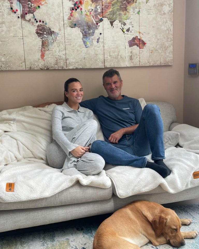 a man and a woman sit on a couch with a map of the world behind them