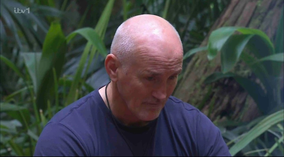 a bald man in a blue shirt is sitting in the jungle on itv1