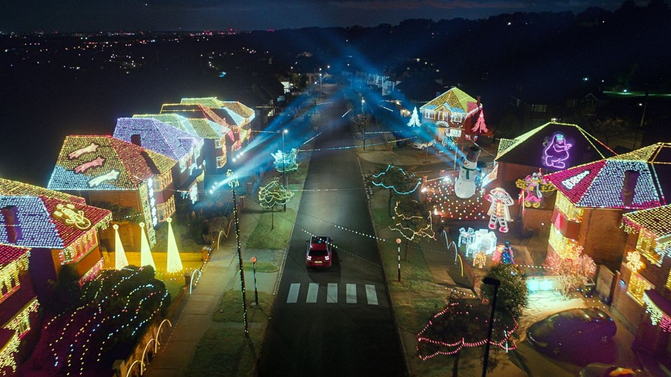 a red car is driving down a street decorated with christmas lights