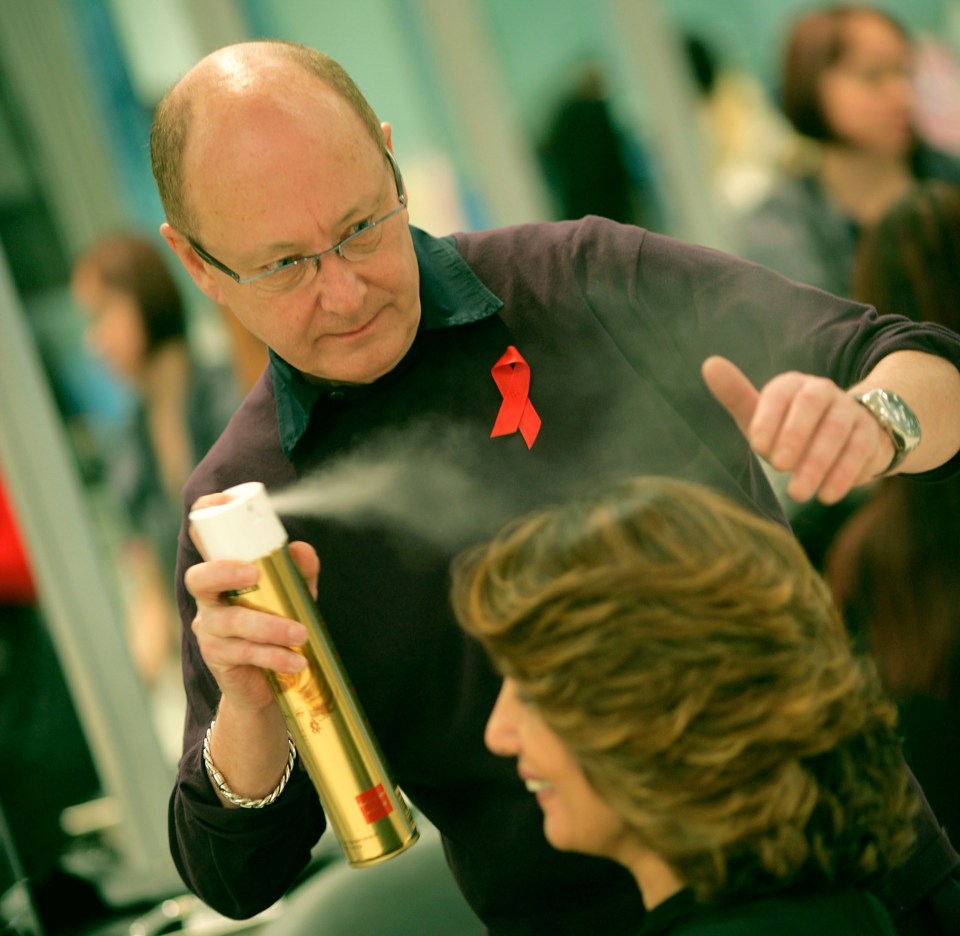 a man with a red ribbon on his shirt is spraying a woman 's hair