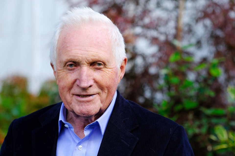 an older man wearing a blue shirt and a black jacket smiles for the camera