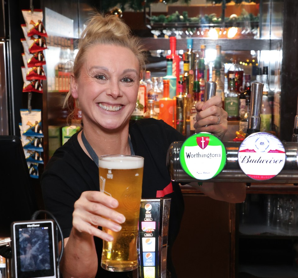 a woman holding a glass of beer next to a budweiser tap