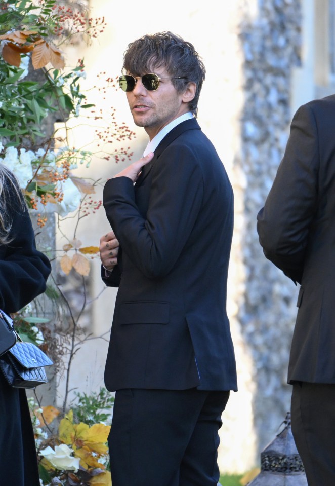 a man in a suit and sunglasses stands in front of a building