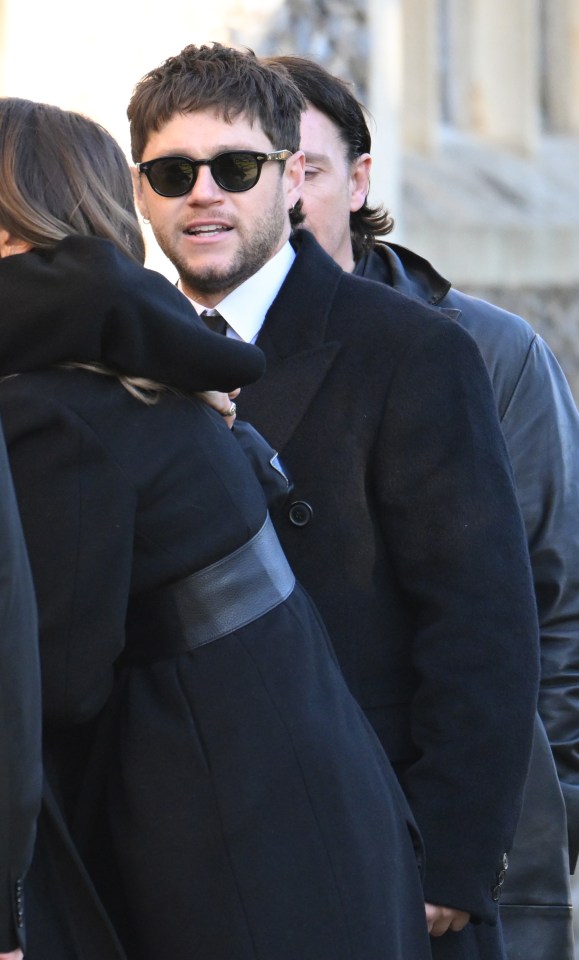 a man wearing sunglasses stands next to a woman in a black coat