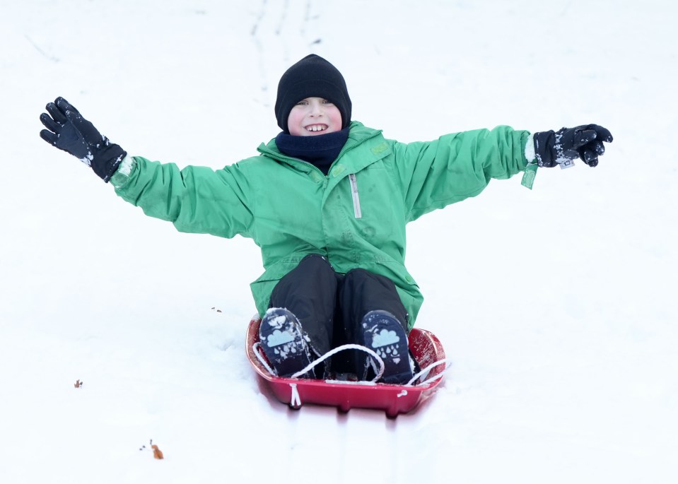 a young boy in a green jacket is sledding down a snowy hill