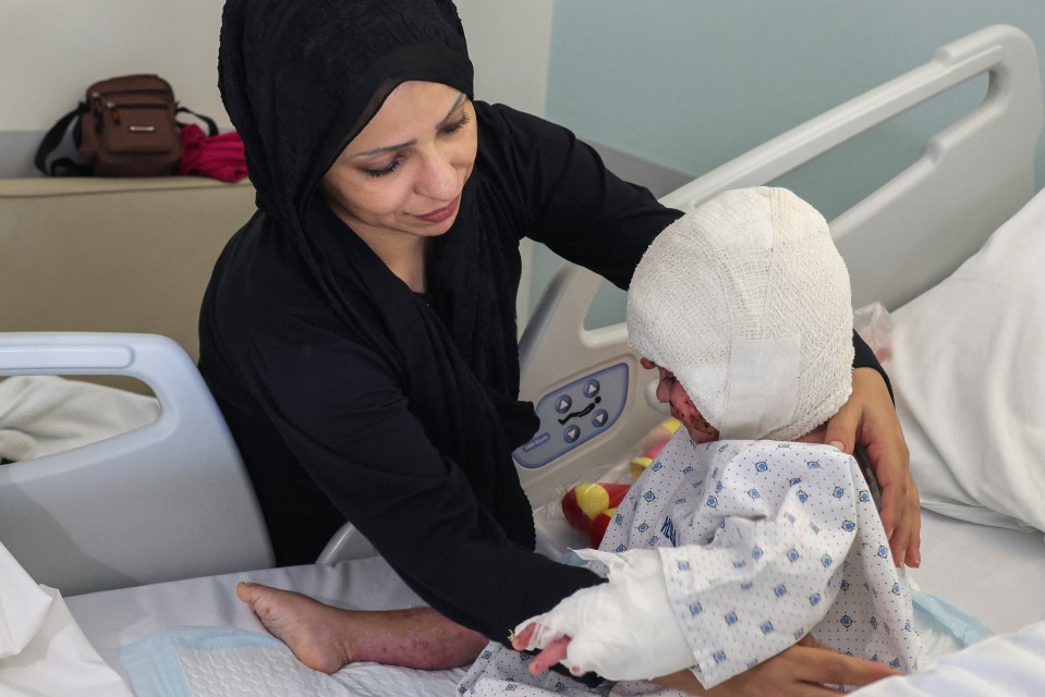 a woman in a black head scarf holds a baby in a hospital bed