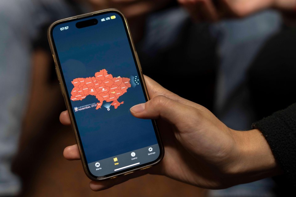 A person in Kyiv is seen holding a smartphone displaying the red warning map