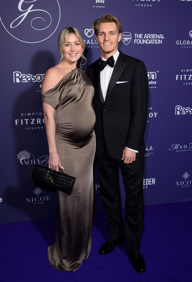 a man and a pregnant woman pose for a photo on a blue carpet that says the arsenal foundation