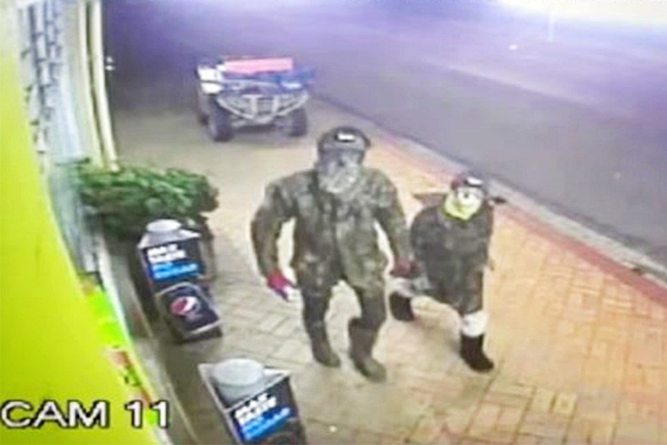 two masked men are walking down a sidewalk next to a atv .