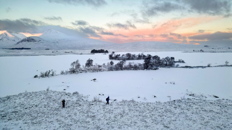 two people standing in a snowy field with mountains in the background