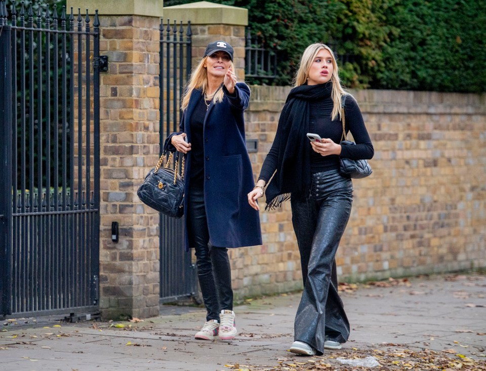 two women are walking down a sidewalk and one is wearing a hat with the letter c on it