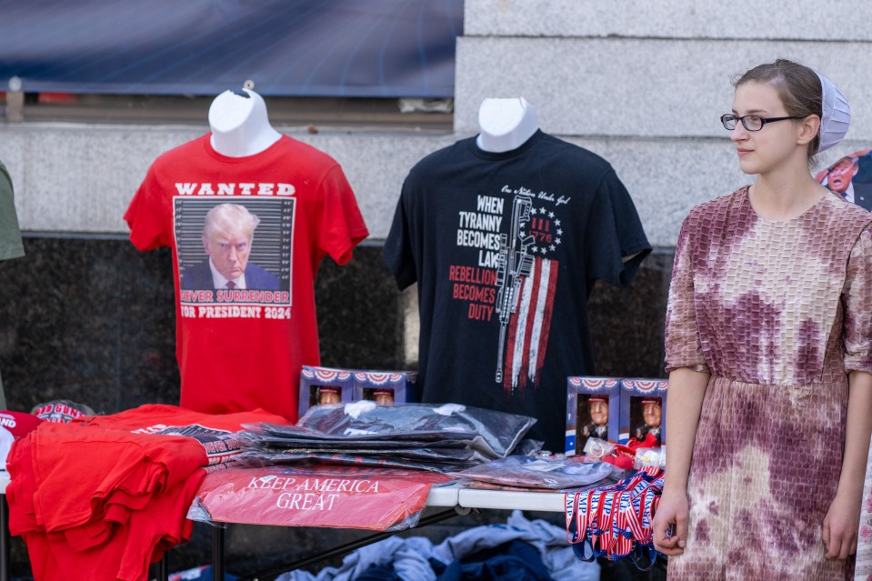 a woman stands in front of a table full of t-shirts including one that says wanted