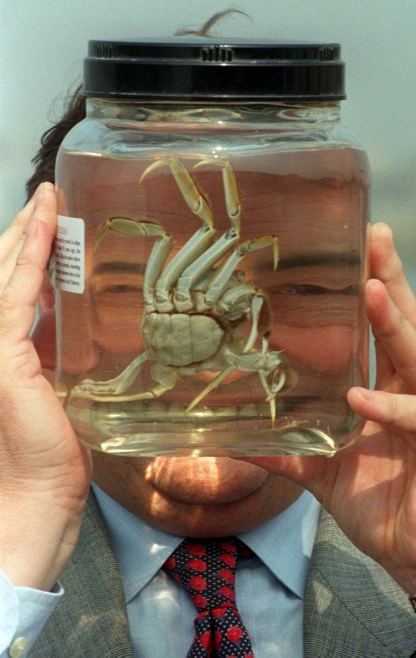 a man in a suit and tie is holding a jar with a crab in it