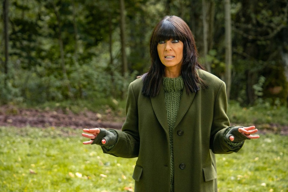 a woman in a green coat is standing in a field with her arms outstretched