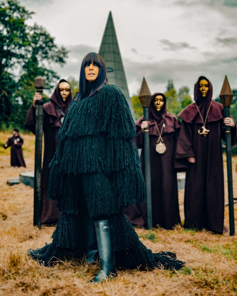 a woman in a black coat stands in front of a group of monks