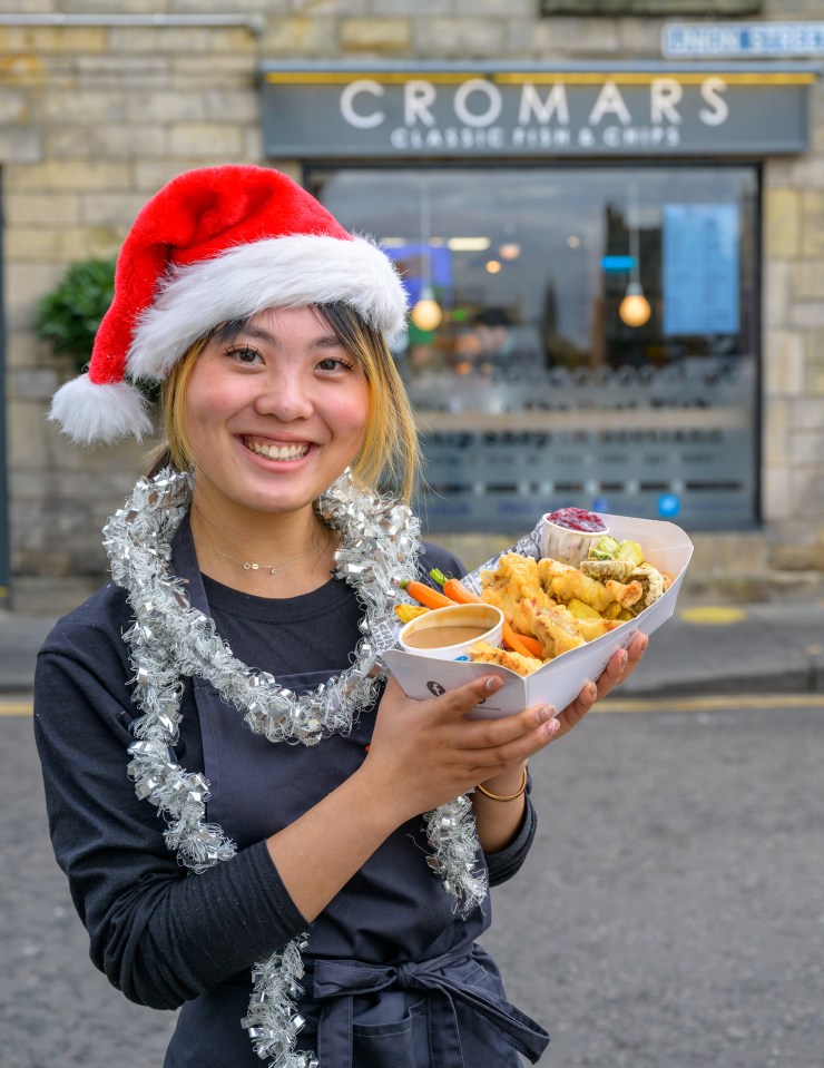 a woman wearing a santa hat is holding a plate of food in front of a store called cromars