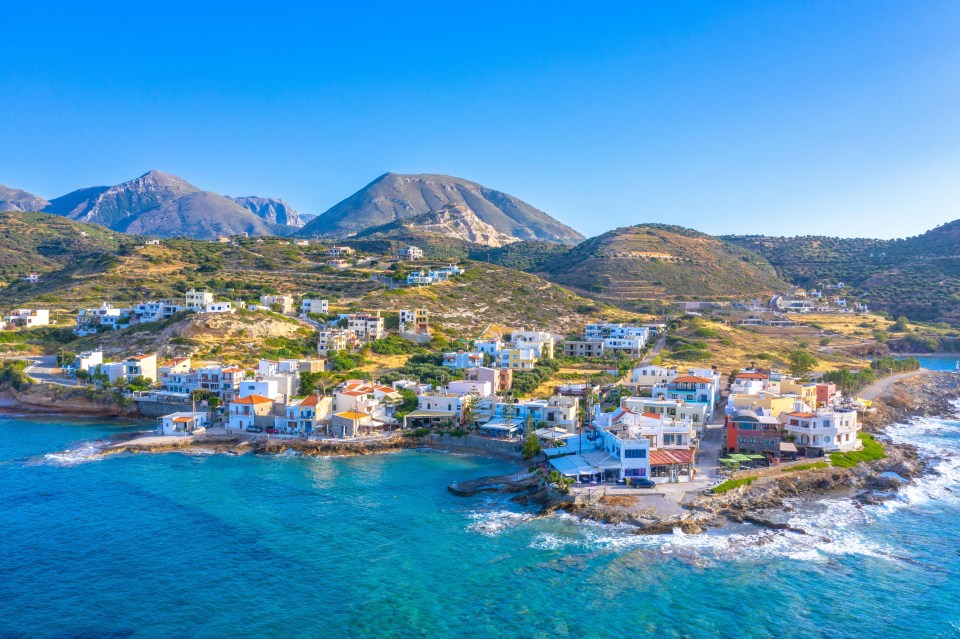 a small town sits on a rocky shoreline with mountains in the background