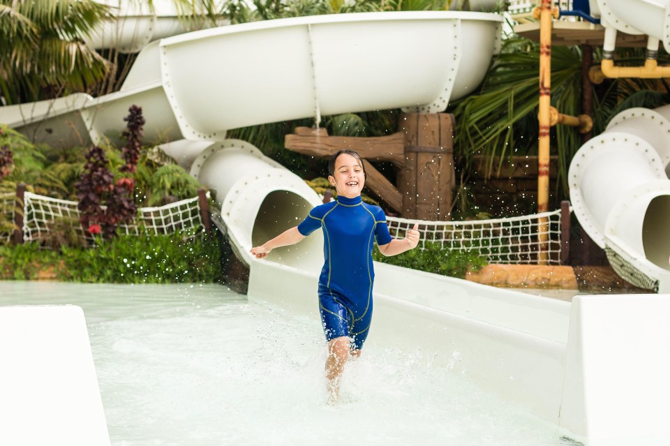 a young girl in a blue wetsuit is running down a water slide