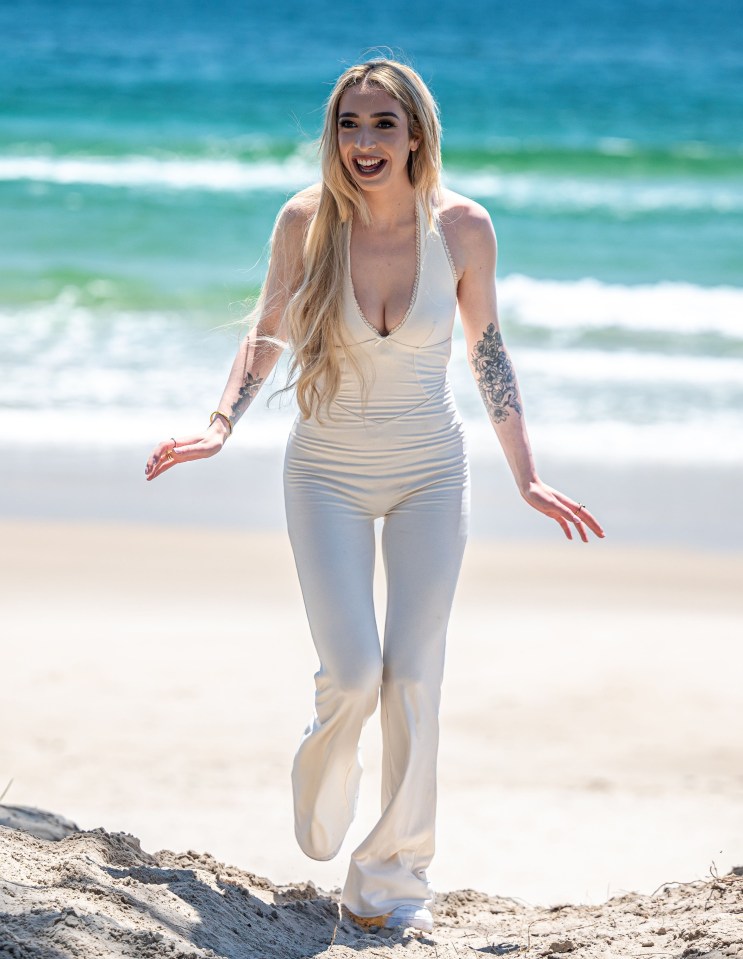 a woman in a white jumpsuit is walking on the beach